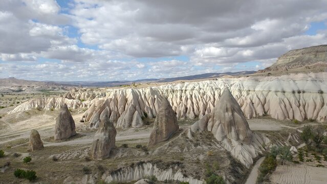 Detailed view of white volcanic tuff ridges and cone-shaped rock formations in Cappadocia valley under a cloudy sky.