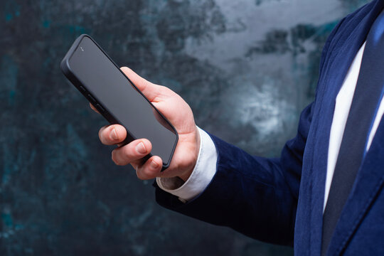 Close up of businessman holding smartphone in office environment. Corporate communication, mobile banking and business technology concept.