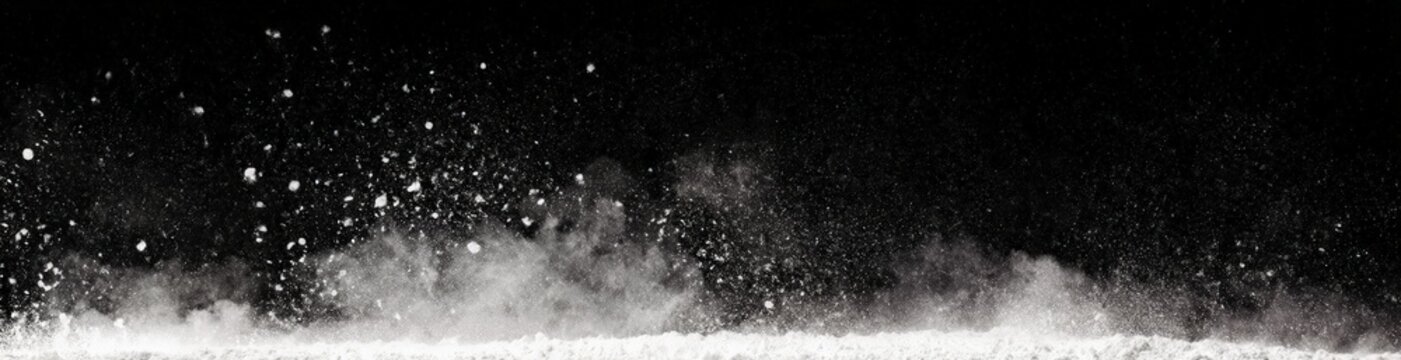 Black and white image showing powdery white dust particles suspended and spreading in the air against a dark background.