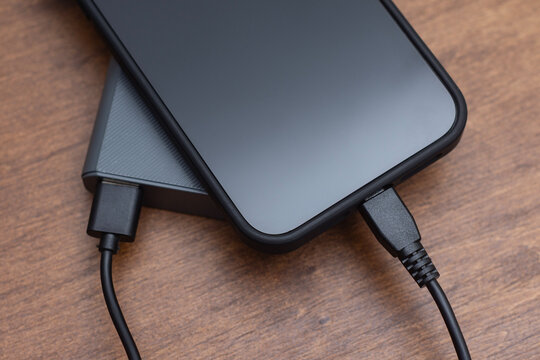 Smartphone charging on power bank with cable on wooden desk.