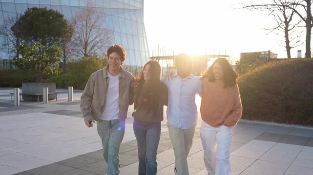 Slow motion of four multi ethnic friends walking together arm in arm. Happy young people laughing and having fun outdoors at sunset