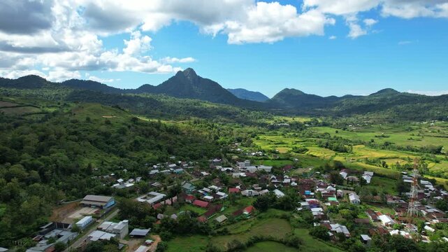 Aerial drone footage of Berang Rea village, with many local houses, in a big valley full of green rice fields, with majestic conic small mountains behind, in Sumbawa regency, Sumbawa island, Indonesia