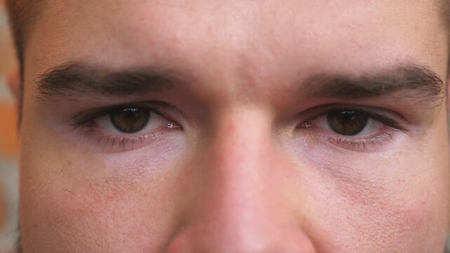 Close up brown eyes of guy staring and blinking with a disappointment sight. Portrait of male face looking into camera. Facial expression of desperate and unhappy man. Dolly shot
