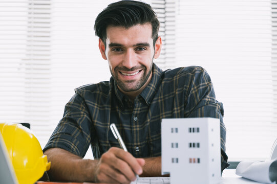 Smiling young architect or engineer working on building design project at office desk with blueprint. Concept of construction business, architecture, engineering, planning, and real estate development