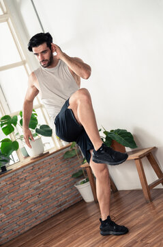 Fit young man doing knee raise exercise during a home workout in a modern living room. Concept of healthy lifestyle, fitness training, cardio exercise, strength balance, wellness, and active indoor ro