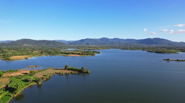 Aerial drone footage of the edge of Batu Bulan water reservoir lake, at sunset, in Sumbawa regency, Sumbawa island, Indonesia, with wild green nature and mountains behind, golden sun rays, quiet water