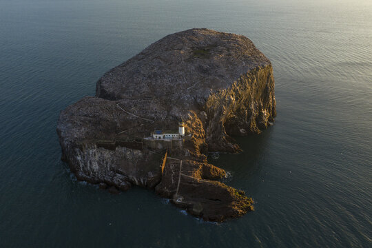Aerial view of Bass Rock Lighthouse and historic ruins on the steep volcanic island surrounded by the blue waters of the Firth of Forth, North Berwick, Scotland, United Kingdom.