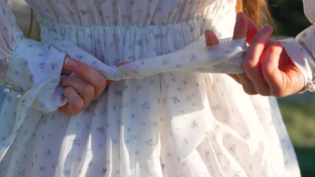 Hands dress bow tying a delicate ribbon on a floral vintage dress in soft sunlight for a graceful look