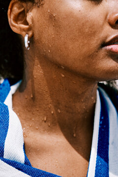 A close-up view of a young woman with water droplets on her skin. She is wrapped in a blue and white striped towel after swimming on a bright and sunny summer day.