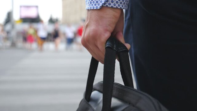 Young businessman holding bag in hand and crossing the road in downtown. Unrecognizable male entrepreneur carry briefcase in arm and walking a crosswalk in big city. Rear view Slow motion Close up