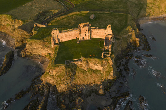 Aerial view of Tantallon Castle ruins perched on a steep cliff overlooking the North Sea during golden hour in North Berwick, Scotland, United Kingdom.