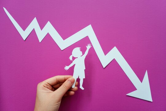 A hand holds a paper cutout girl under a declining graph on pink
