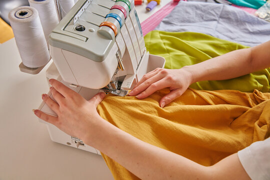 Professional seamstress hands using an overlock sewing machine on orange fabric in a workshop
