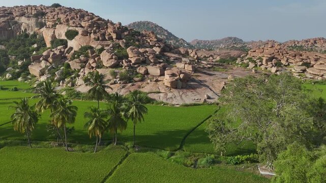 Aerial 4K drone footage of Hampi in Karnataka India. Cinematic bird's eye view of rice fields and boulder-strewn landscape.