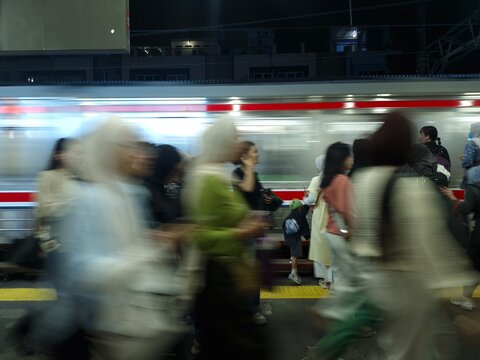 A dynamic long-exposure shot of a crowded train station platform at night, featuring the motion blur of commuters and a passing train. The image captures the fast-paced urban life and daily rush hour.
