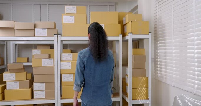 Asian woman entrepreneur slowly opens both hands present successful e-commerce operation with warehouse parcel boxes representing online business readiness, communicating positive e-commerce service