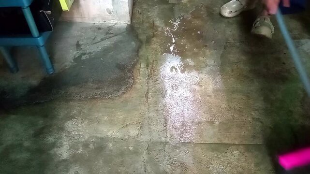 Person using pink squeegee to sweep water on concrete floor