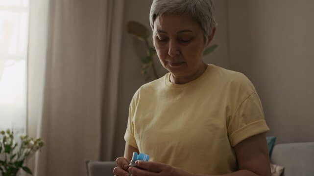 Tilt up shot of senior woman preparing CGM applicator before applying glucose sensor onto body during diabetes daily management at home