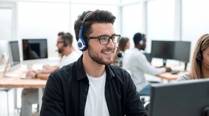 Obraz premium Friendly young male customer service representative wearing headset and glasses working in modern bright office environment with colleagues in background providing professional client support