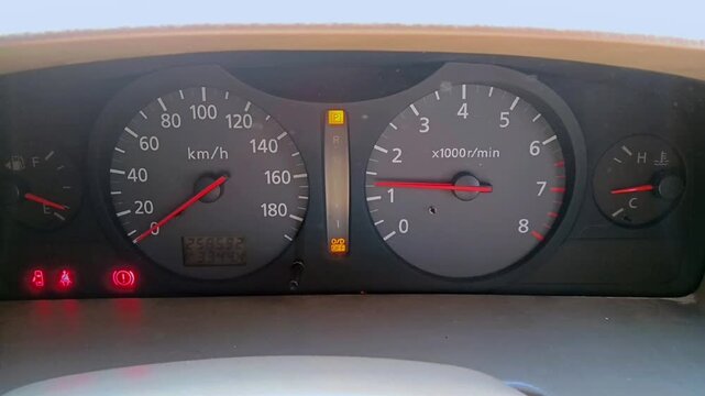 A car instrument cluster shows grey speedometer and tachometer dials, fuel and temperature gauges, red warning lights, a park indicator, and an odometer display on the black panel.