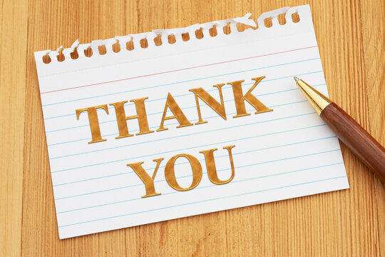 Thank you text on a torn index card with a pen on wood desk