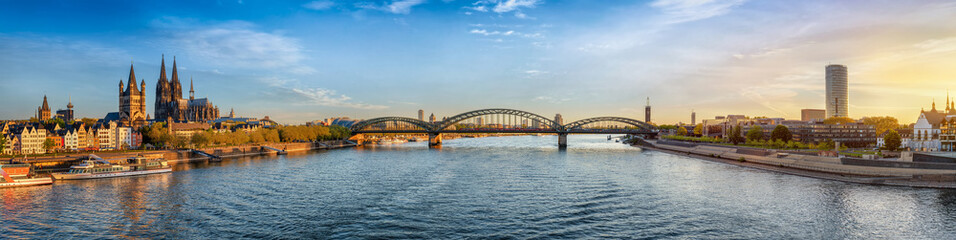 Panoramic view of the skyline of Cologne, Germany, stretching from the old town and Cathedral over the River Rhine to the east side during a golden summer sunrise © moofushi