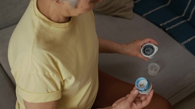 High angle close up shot of middle aged woman inspecting CGM applicator for safe use while continuous glucose monitoring routine at home