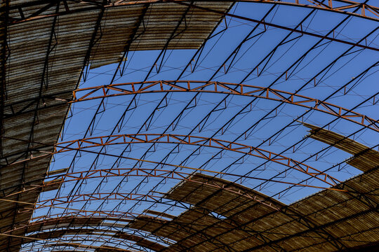 Curved Steel Roof Structure of Abandoned Industrial Warehouse Against Blue Sky
