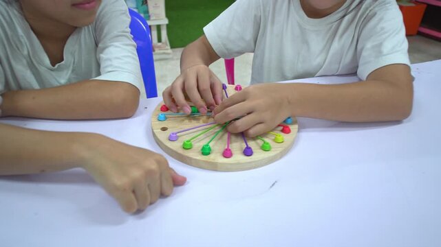 Close up of children's hands playing with a colorful wooden stringing toy, practicing fine motor skills and hand-eye coordination.