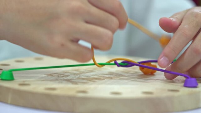 Close up of children's hands playing with a colorful wooden stringing toy, practicing fine motor skills and hand-eye coordination.