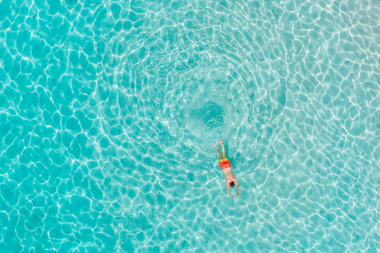 Aerial view of a person swimming in crystal clear turquoise water with sunlight reflecting on the surface in Innafinolhu, Haa Alif Atoll, Maldives.