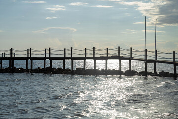 Obraz premium Wooden pier silhouette over shimmering sea water with bright sun trail under cloudy sky. Side, Turkey, Mediterranean.