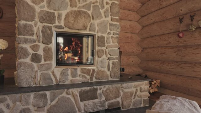 Flames burning in a modern stone fireplace inside a rustic wooden chalet living room during winter