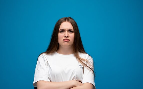 Young woman reacting with disgust or displeasure, frowning with arms crossed against a blue studio background