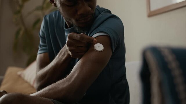 Close up on young adult Black man adjusting adhesive patch on upper arm after applying glucose monitor sensor during daily diabetes care at home
