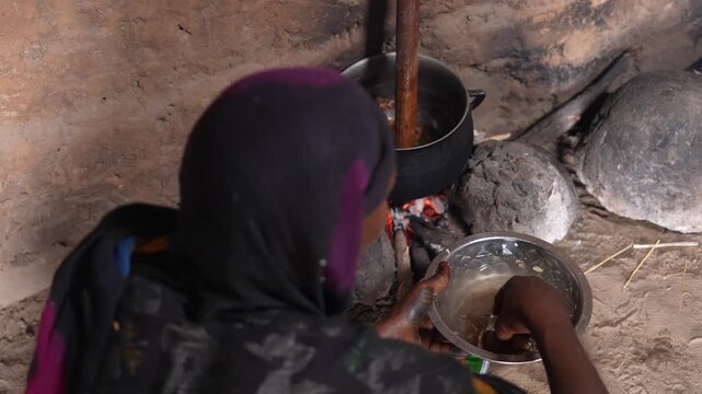 African woman adding ingredients into pot for traditional village meal, April 25, 2026, Chad, N Djamena
