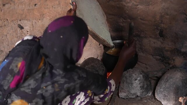 African woman adding ingredients into pot for traditional village meal, April 25, 2026, Chad, N Djamena
