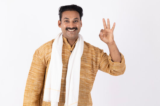 Portrait of smiling young indian farmer wearing kurta pajama, gesturing and looking at the camera while standing against white background
