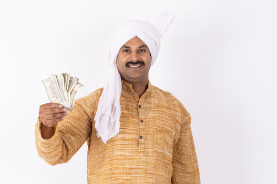 Portrait of smiling young farmer showing indian rupees currency wearing kurta pajama and white turban gesturing while standing against white background