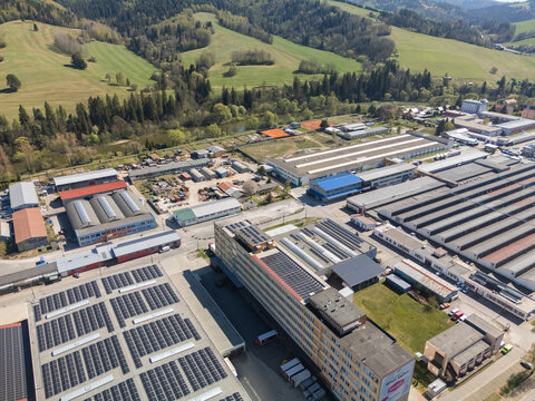 Aerial view of an industrial complex with solar panels on rooftops and surrounding green hills in Nizna, Zilina Region, Slovakia.