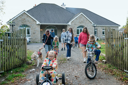 Girl with ponytails riding a toy car with her family walking behind her