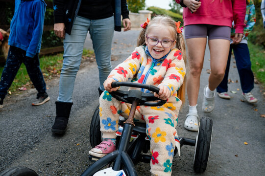 Girl with ponytails riding a toy car with her family walking behind her