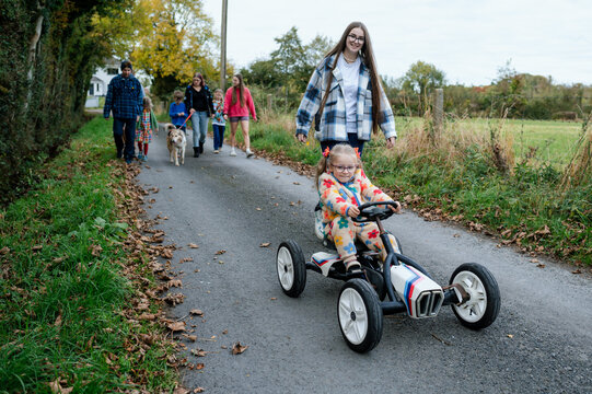 Girl with ponytails riding a toy car with family walking behind