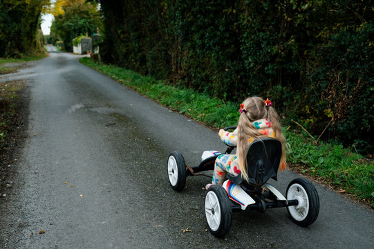 Girl with ponytails riding a toy car on countryside road