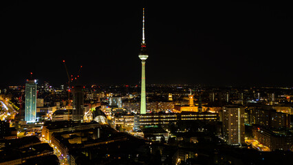 Drone aerial view of the Fernsehturm Berlin TV Tower and Alexanderplatz at night, Berlin-Mitte, Germany. High angle shot of the illuminated city skyline and modern architecture under a clear sky. © Cirrus Height