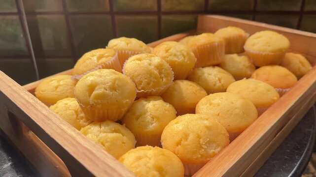 Video of fresh vanilla cupcakes in wooden tray with fluffy texture and warm bakery ambiance