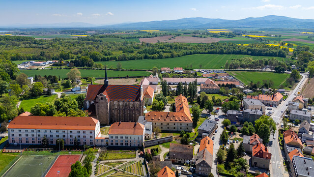High-angle aerial shot of the Cistercian Abbey in Henryk&oacute;w, Lower Silesia, featuring the ornate baroque monastery complex, church towers, red-tiled roofs, surrounding green farm fields, and distant mo