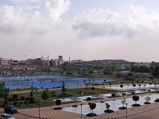 Obraz premium Panoramic vista of a modern university campus with sprawling green spaces, sports courts, and futuristic architectural buildings under a partly