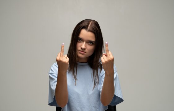 Young woman showing middle finger gesture expressing anger, defiance and disrespect on a gray background