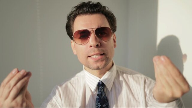Expressive businessman in sunglasses gesturing and talking emotionally to the camera.